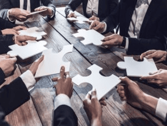 Manos trabajando en rompecabezas corporativo y colaboración empresarial.